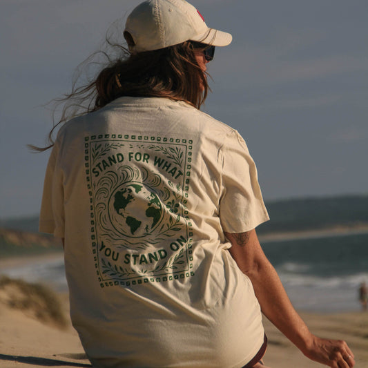 Person sitting on a beach wearing a white t-shirt with a graphic design.