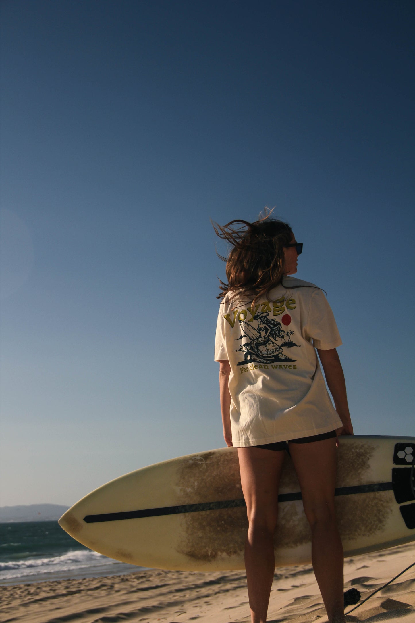 Person holding a surfboard on a beach with a clear blue sky