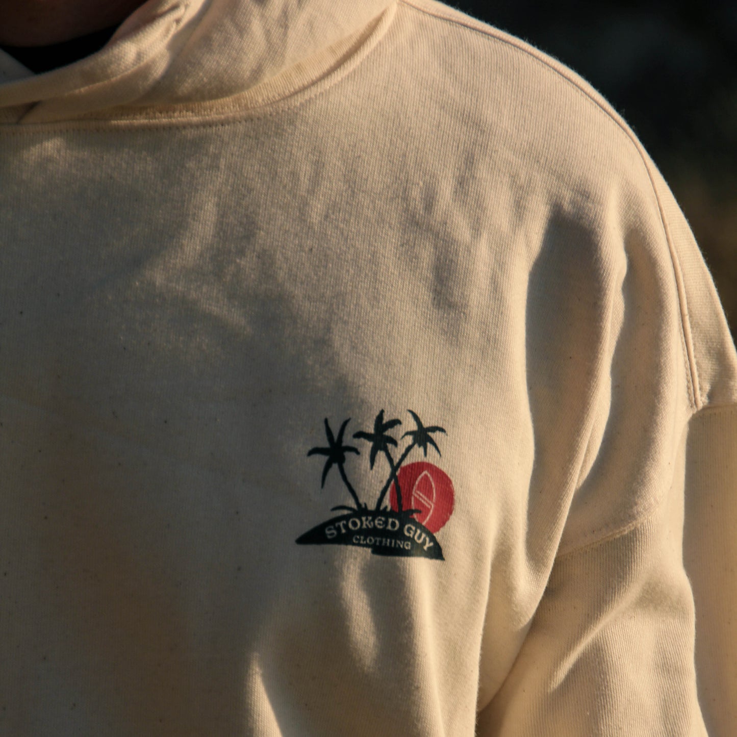 Collage of a beige shirt with a logo featuring palm trees and a red circle, set against a dark background.