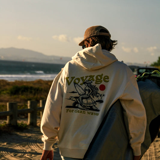 Person wearing a hoodie with 'Voyage' branding on a beach