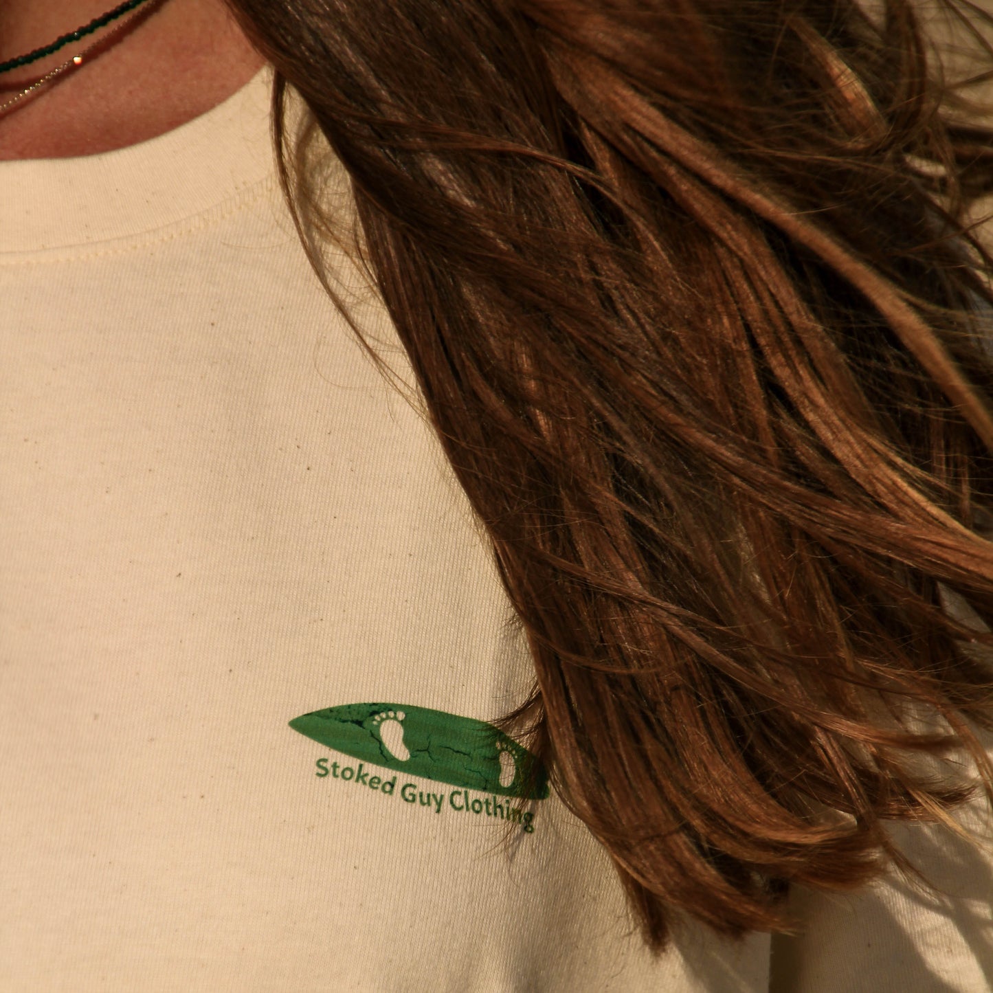 Close-up of a beige t-shirt with a green logo on the chest.