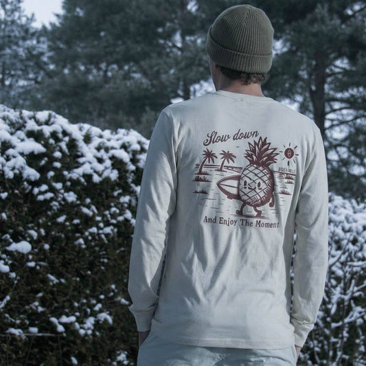 Person wearing a light gray long-sleeve shirt with a pineapple graphic and text, standing in a snowy landscape.