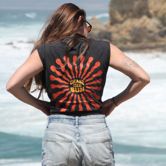 Person wearing a sleeveless shirt with a sun design and text at the beach