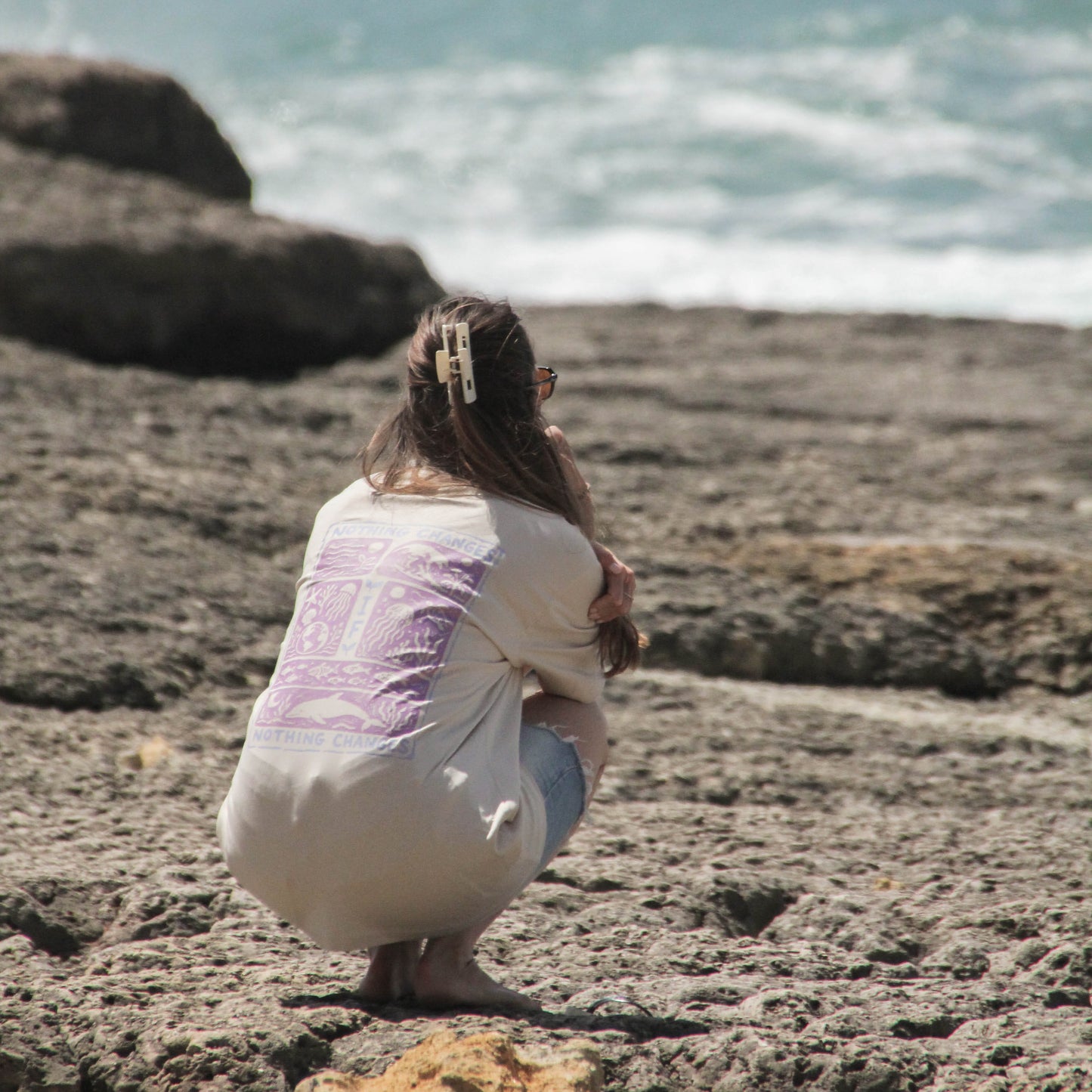 Person sitting on a rocky beach looking at the ocean