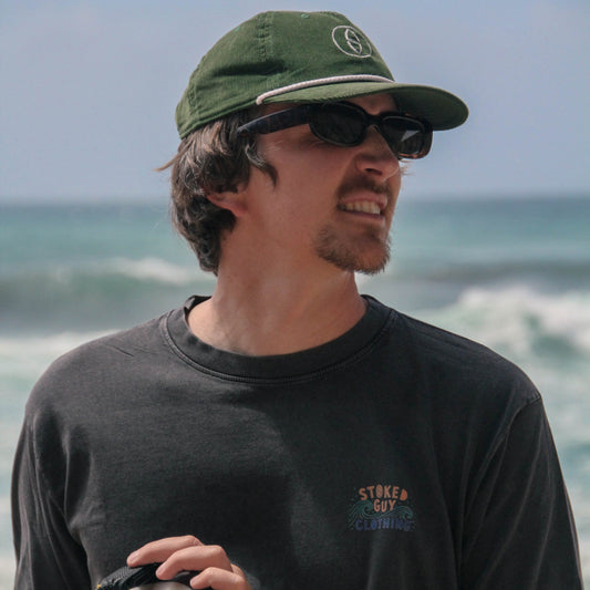 Man wearing a green cap and sunglasses with ocean in the background