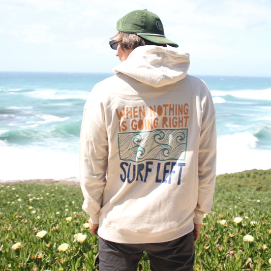 Person wearing a hoodie with text and graphics, standing outdoors near a waterfall.