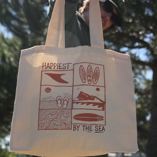 White tote bag with red design and text held by a person outdoors