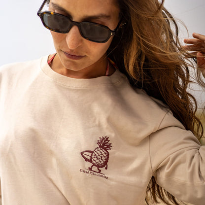 Person wearing a beige long-sleeve shirt with a pineapple logo and text.
