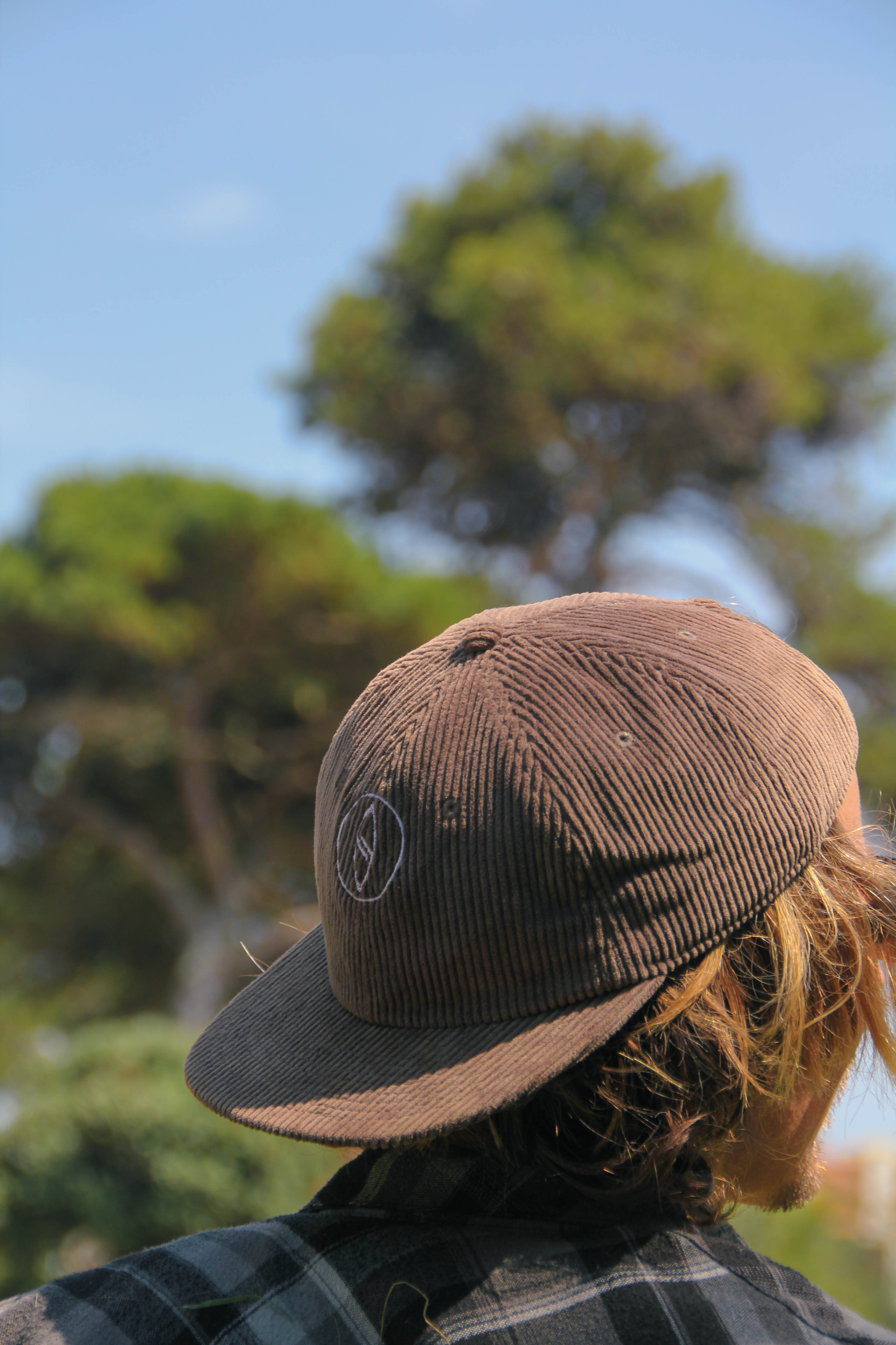 Person wearing a brown and black cap with trees in the background