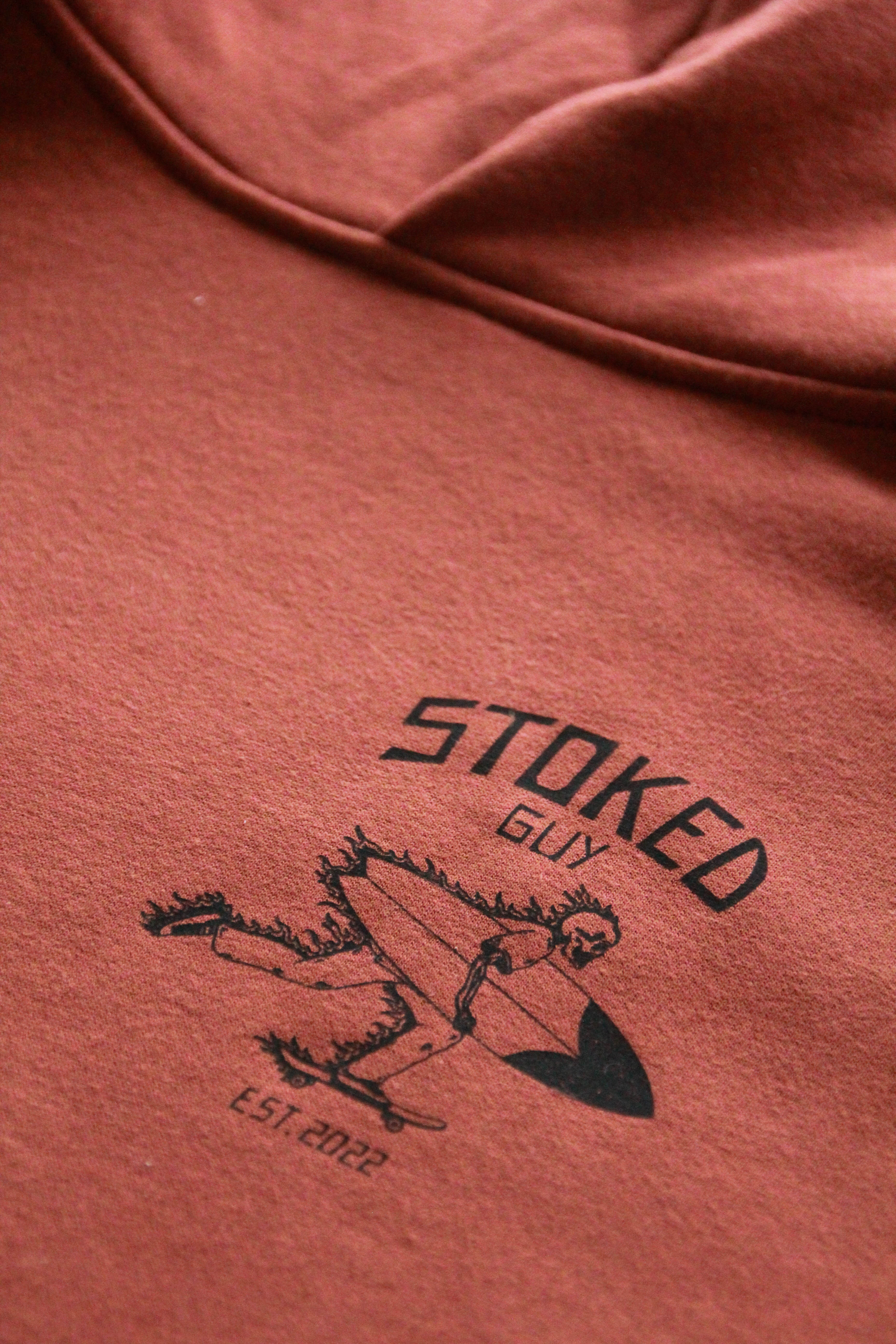 Red hoodie with 'Stoked Guy' logo and text on a close-up of the fabric.