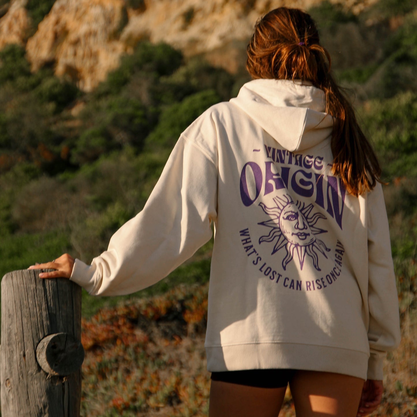Person wearing a hoodie with text and graphics, standing on a cliffside path.