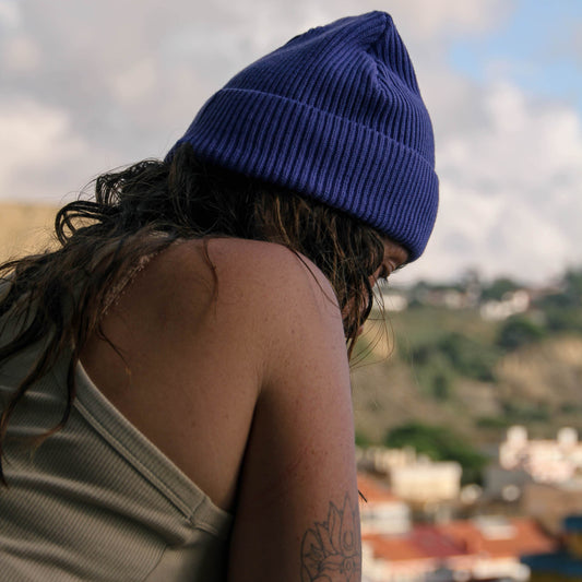 Person wearing a blue beanie looking over a scenic landscape with buildings and greenery.