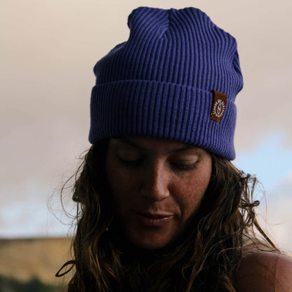 Person wearing a blue beanie with a logo against a neutral background