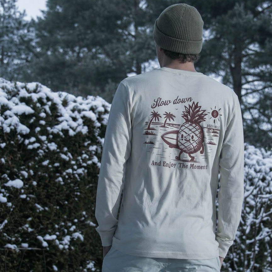 Person wearing a light gray long-sleeve shirt with a pineapple graphic and text, standing in a snowy landscape.