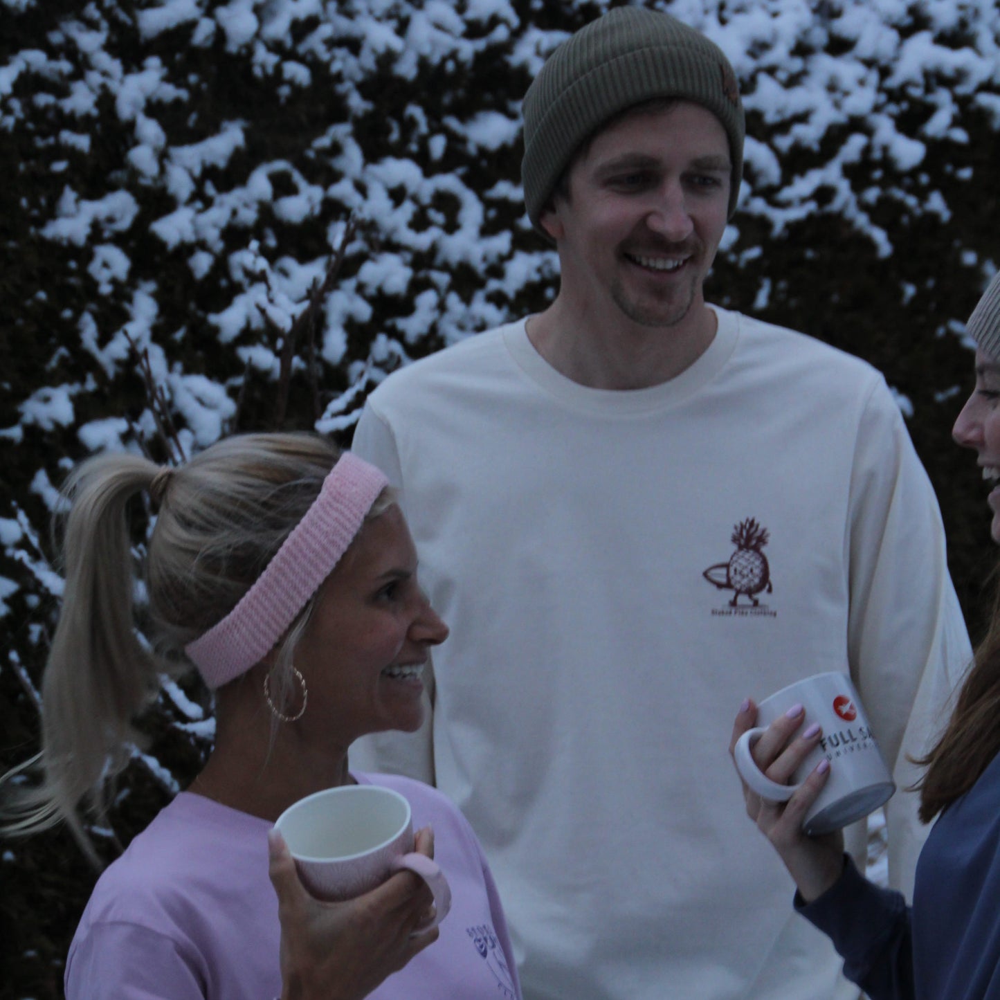 Two people standing outdoors in a snowy setting, holding mugs.