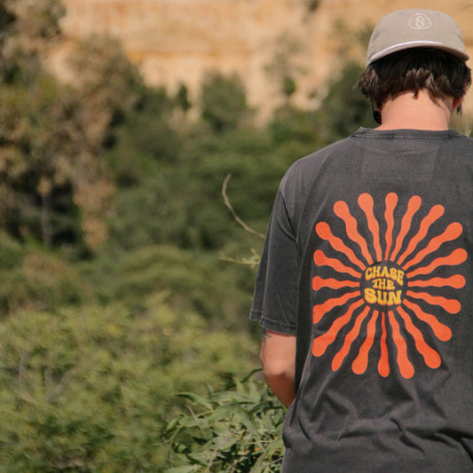 Person wearing a gray t-shirt with a red and orange design, standing in a natural landscape.
