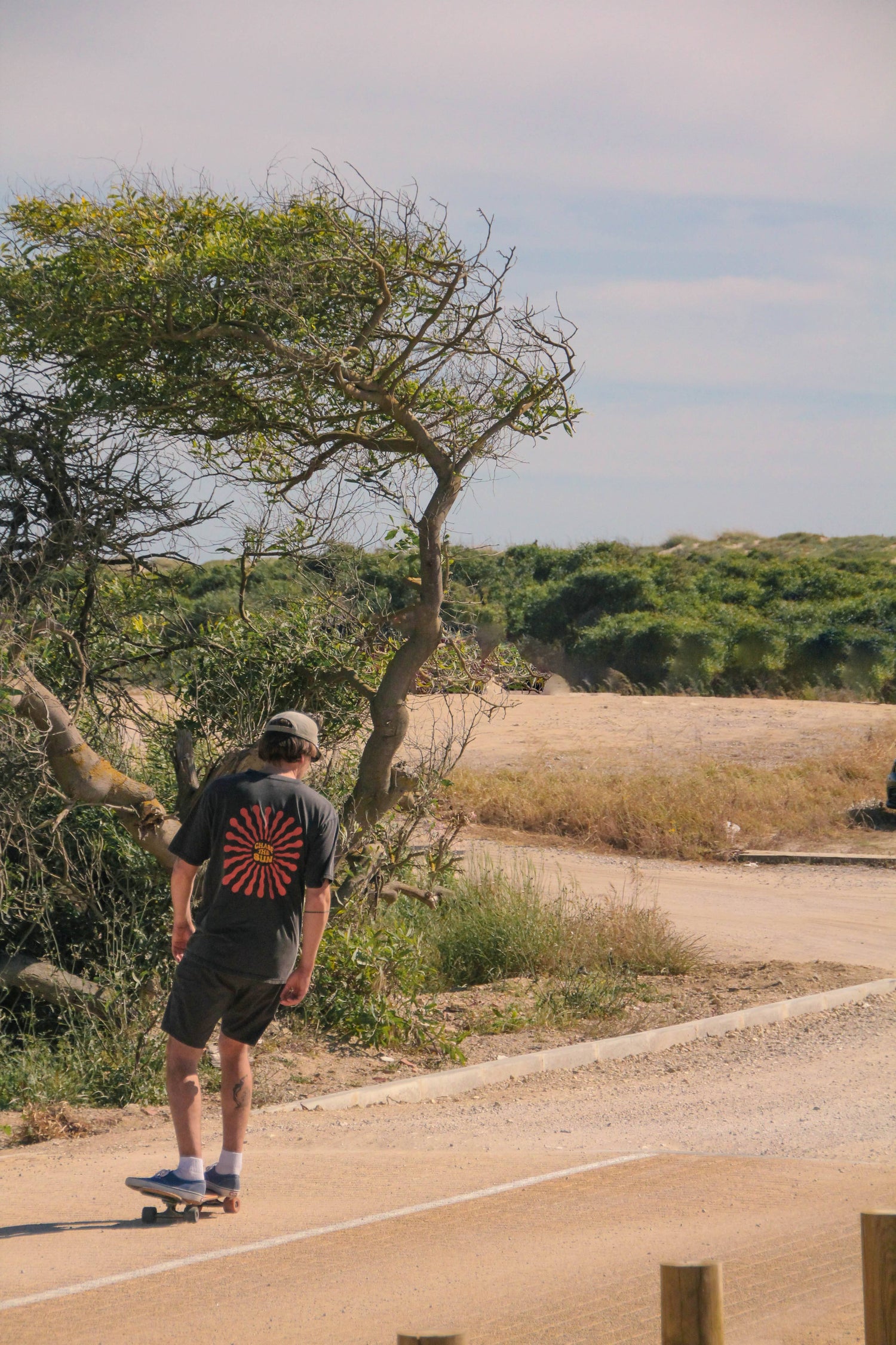 Person skateboarding on a road with trees and open sky in the background