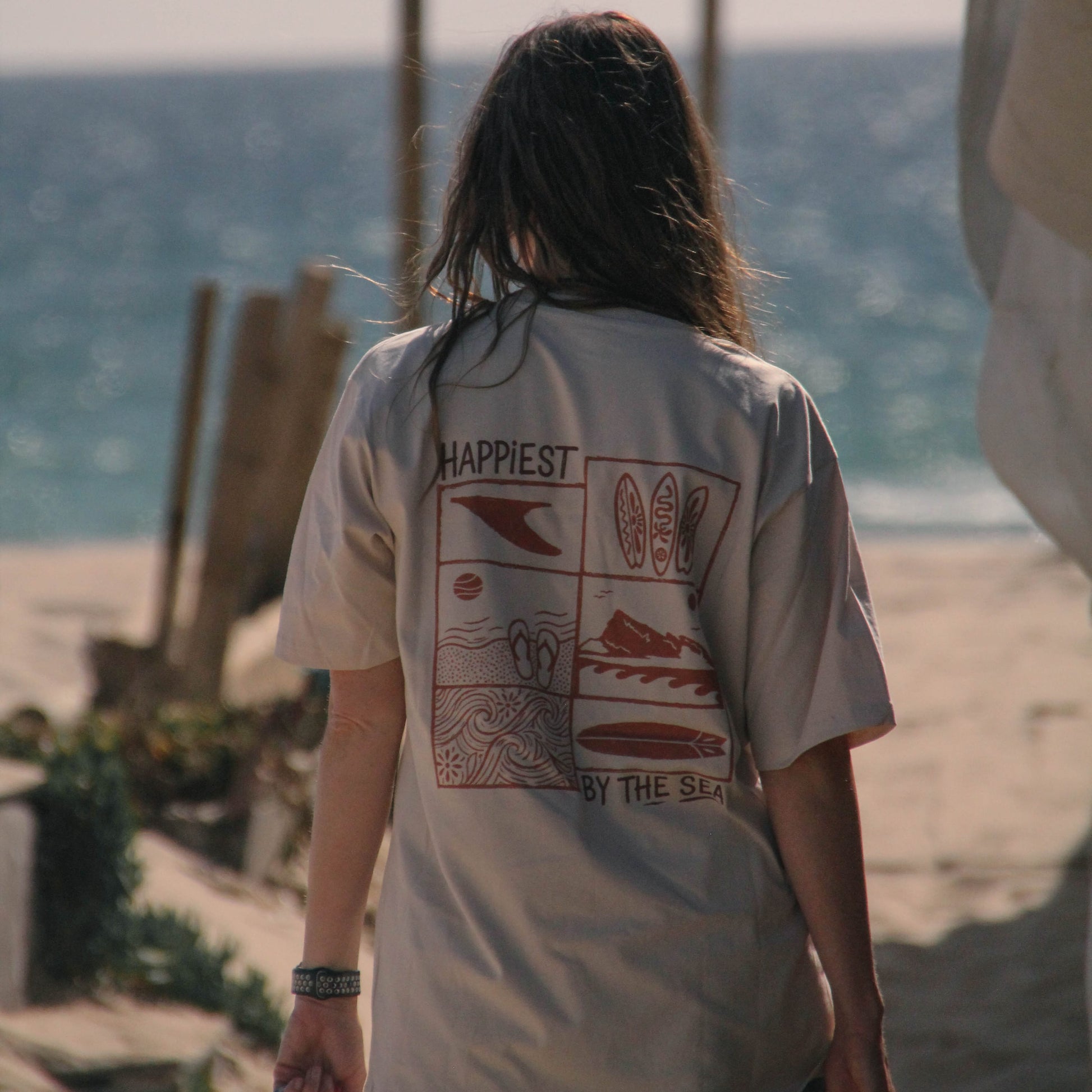 Person wearing a t-shirt with beach-themed graphics and text on a beach.