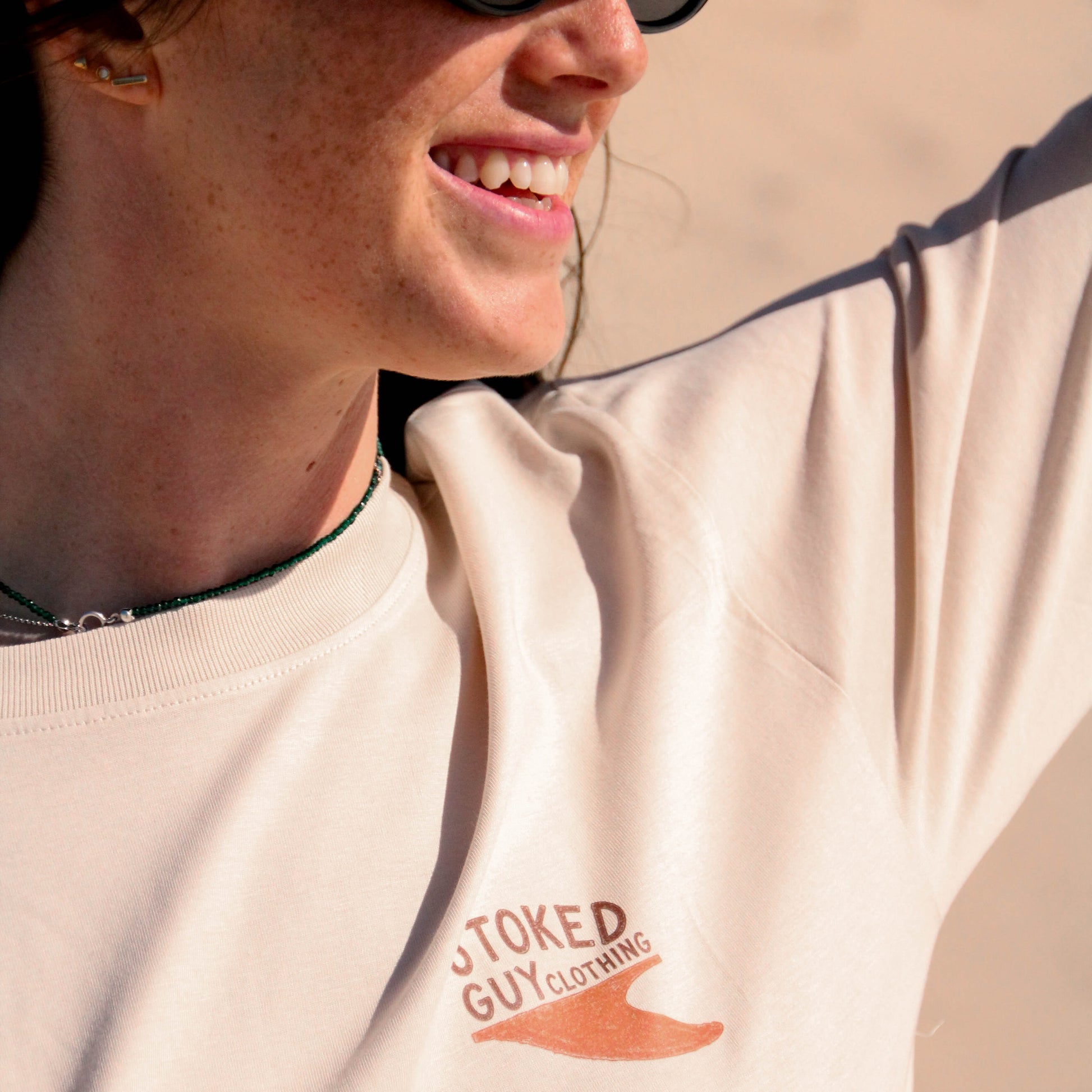 Person wearing a beige sweatshirt with 'Toked Guy Clothing' logo, smiling outdoors.