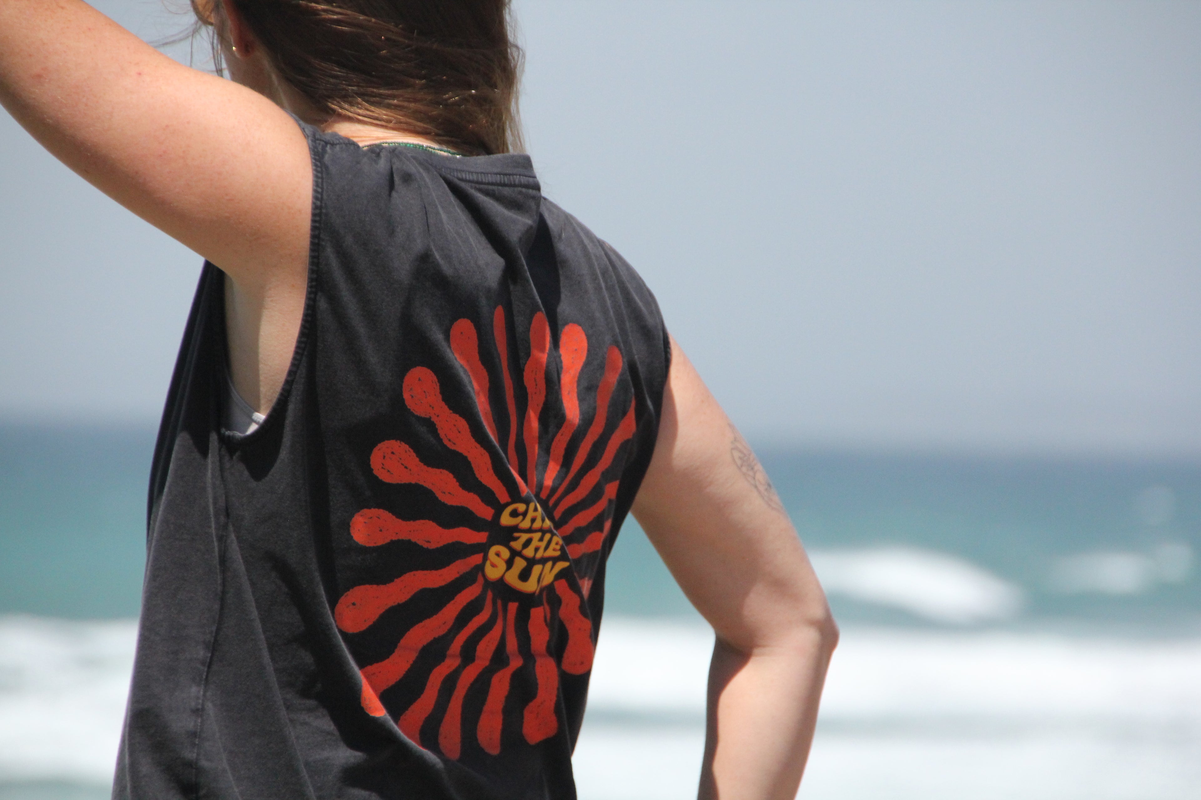 Person wearing a black sleeveless shirt with a red and yellow design on the beach