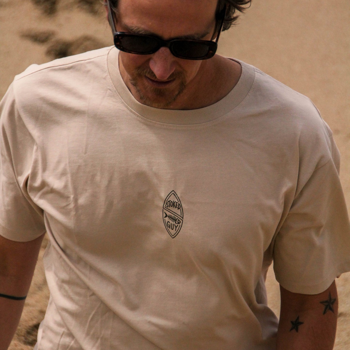 Man wearing a beige t-shirt with a logo in a desert setting