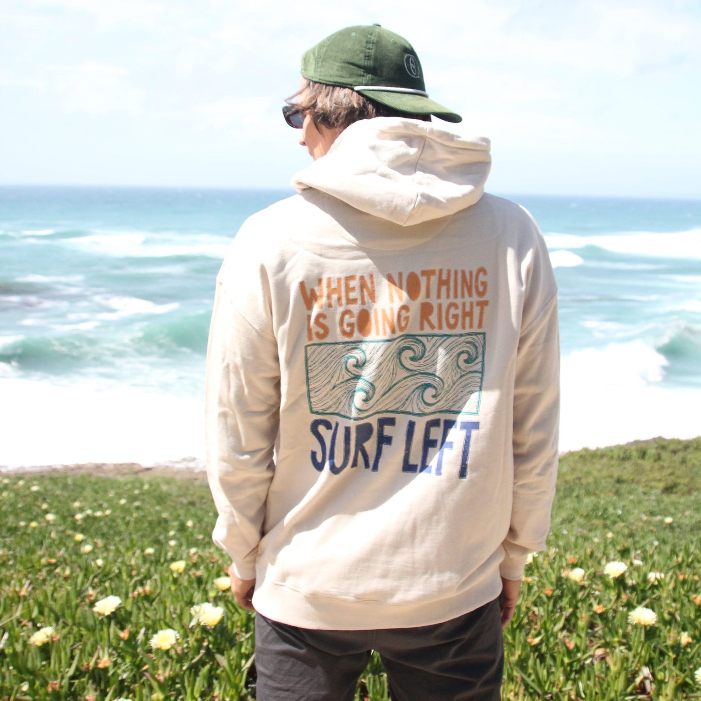 Person wearing a hoodie with text and graphics, standing outdoors near a waterfall.