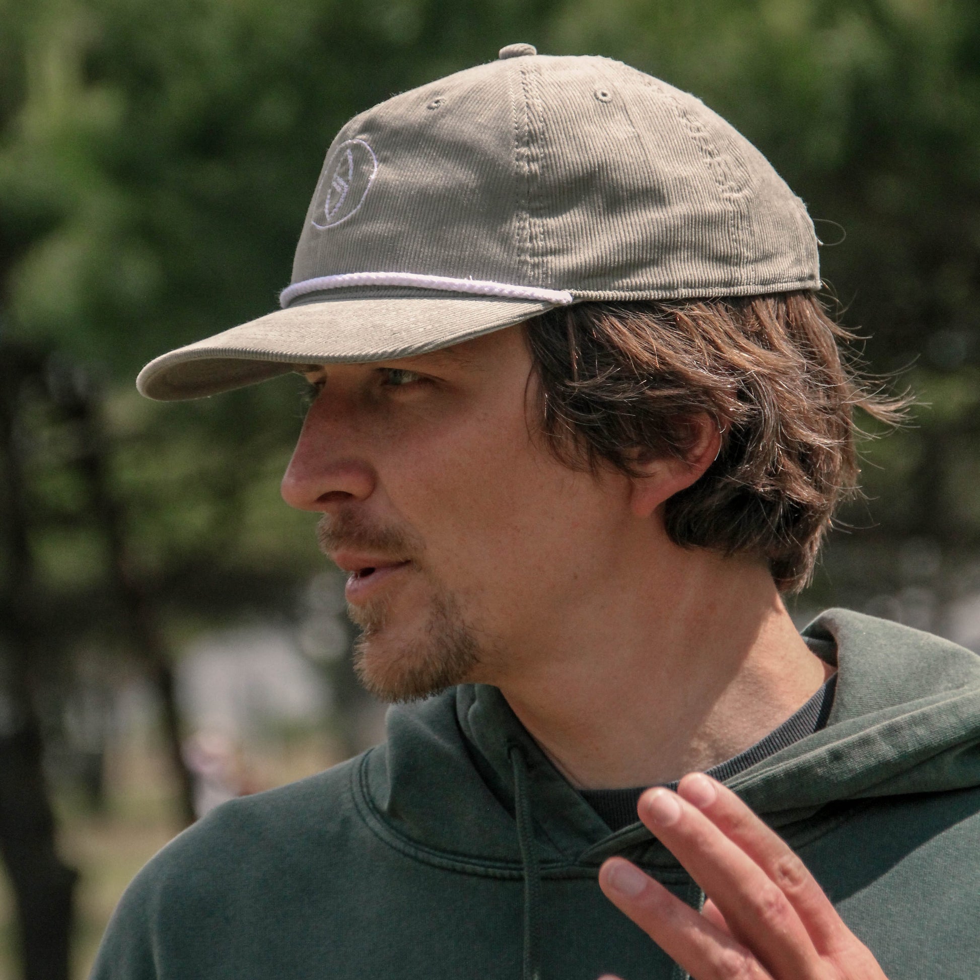 Man wearing a cap and green hoodie outdoors with blurred trees in the background