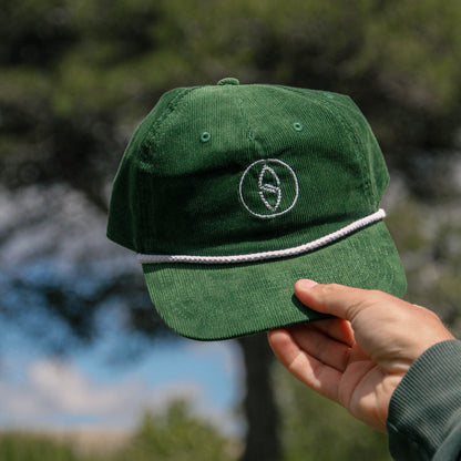 Green cap with a logo held by a hand against a blurred natural background
