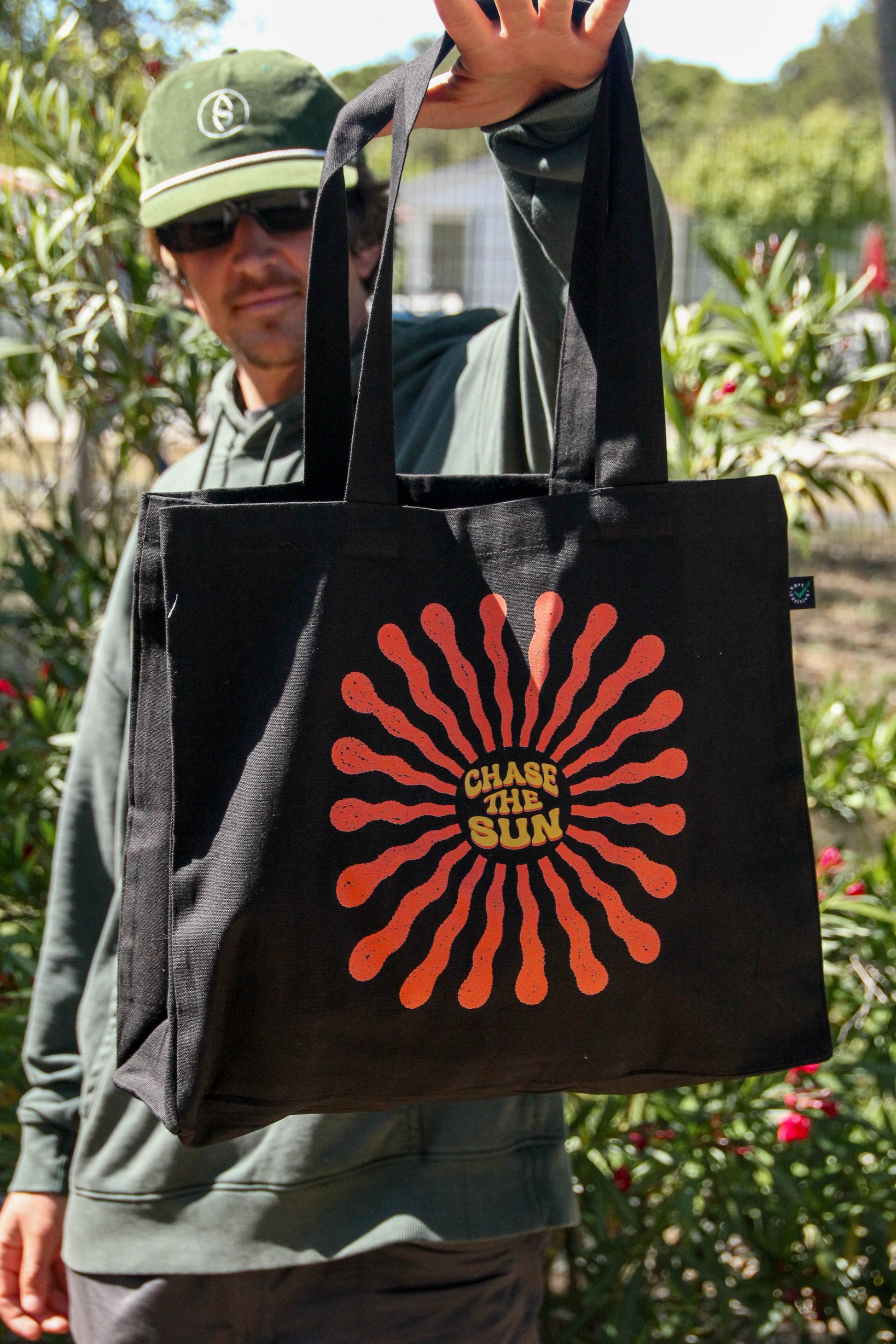 Person holding a black tote bag with a red sun design and 'Chase the Sun' text.