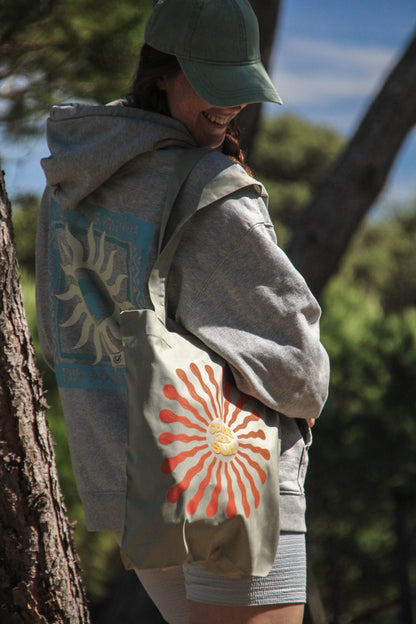 Person wearing a gray hoodie with a sun design and a matching bag outdoors.