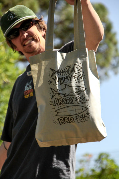 Person holding a tote bag with fish illustrations and text outdoors