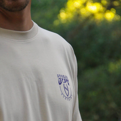 A close-up of a person wearing a cream-colored t-shirt with a blue 'STURGES CUP' logo on the left chest, set against a blurred green outdoor background.