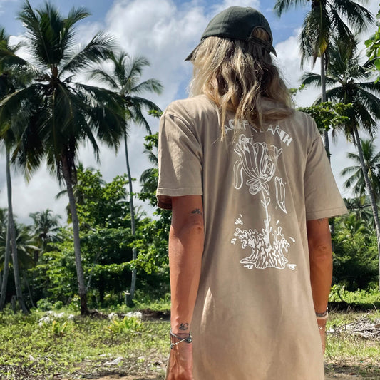 Person wearing a beige t-shirt with a floral design in a tropical setting with palm trees.