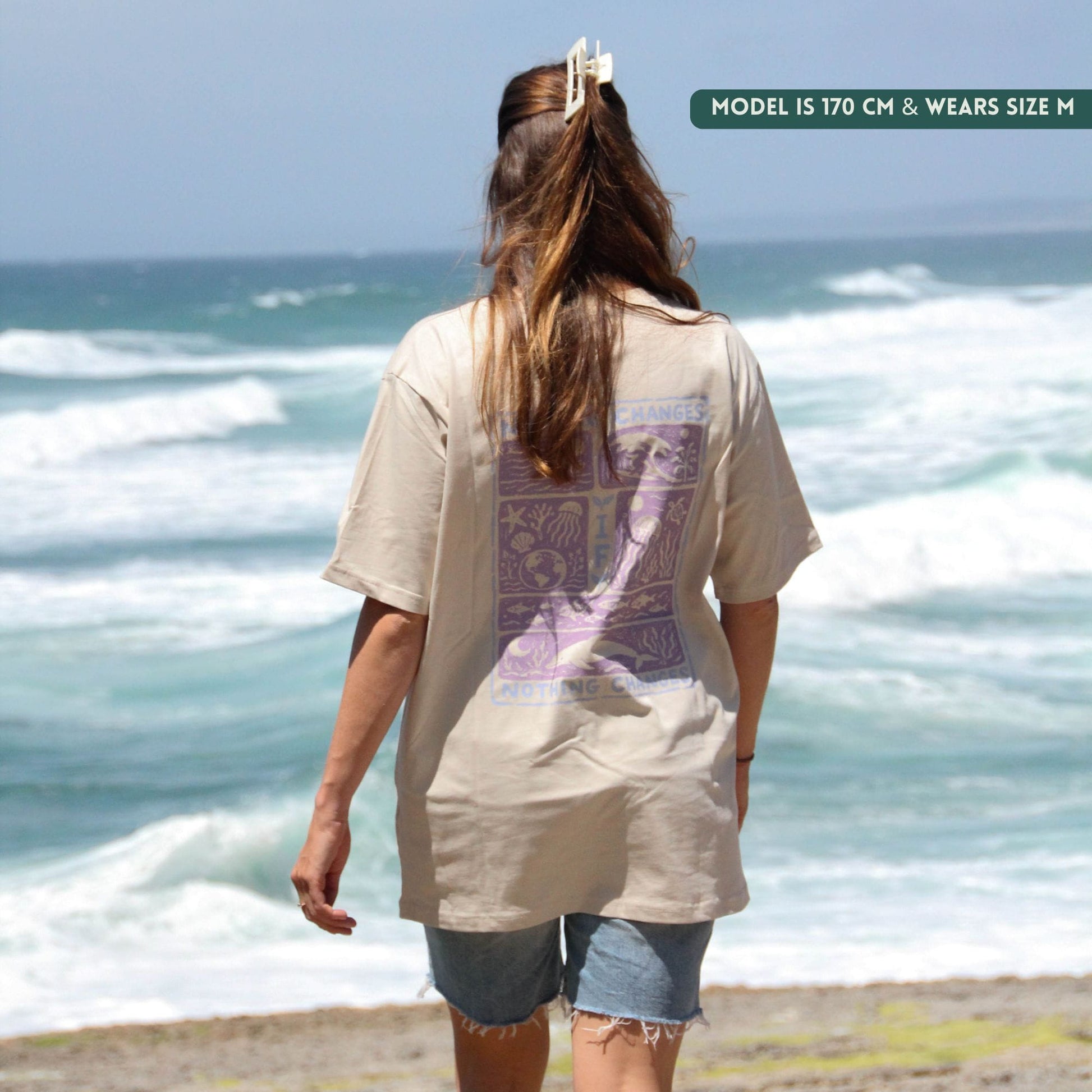 Person wearing a beige t-shirt with a graphic design standing on a beach.