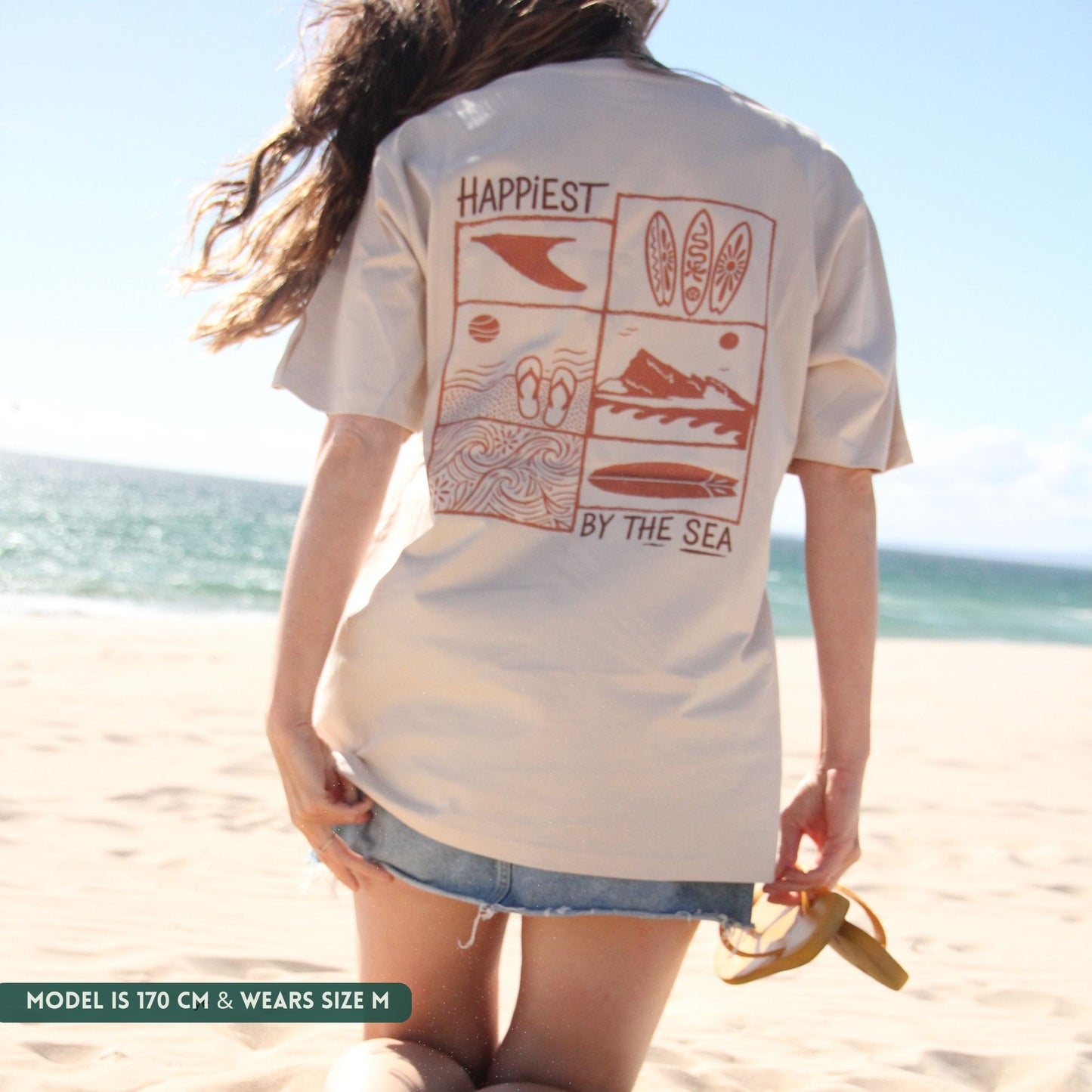 Person wearing a white t-shirt with beach-themed graphics and text on a beach.