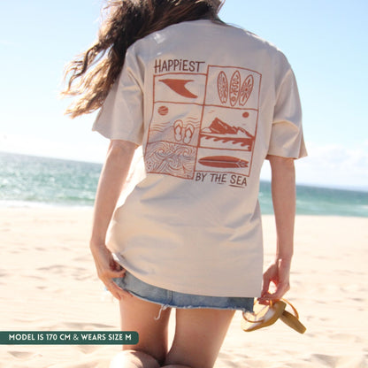 Person wearing a white t-shirt with beach-themed graphics and text on a beach.