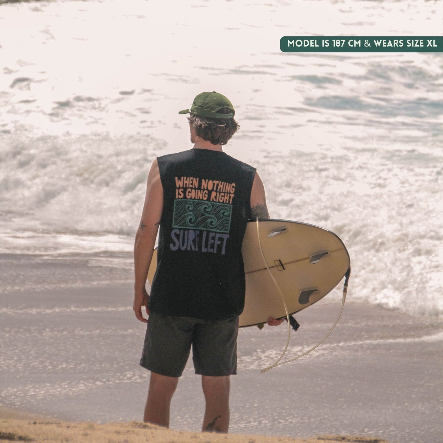Person holding a surfboard on a beach with text on their sleeveless shirt.