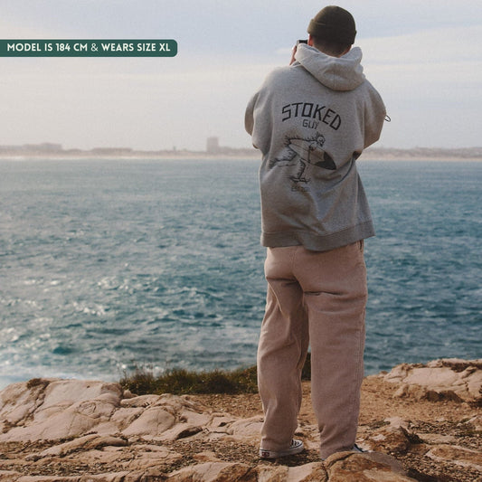 Person wearing a hoodie with 'Stoked Guy' text by the ocean